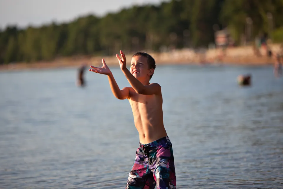 A young boy standing in the water catching a frisbee.