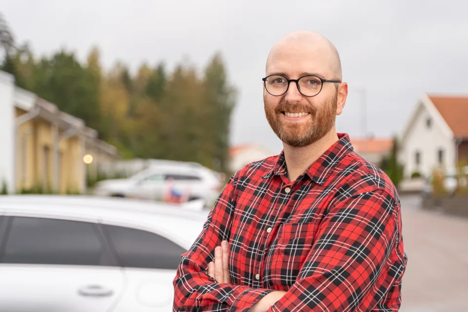 En man som står framför en parkerad bil.