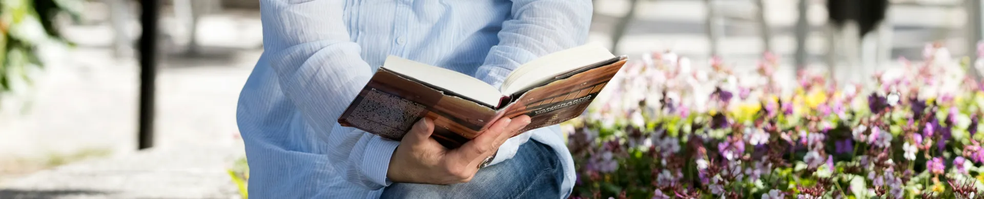En kvinna som sitter på en bänk och läser en bok.