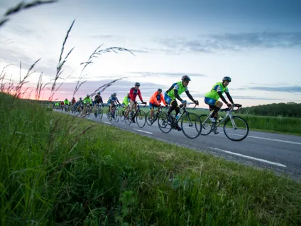Cyklister på landsväg. En himmel som är blå och röd.