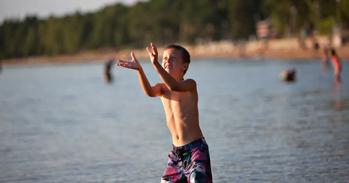 En liten pojke som står i vattnet och fångar en frisbee.