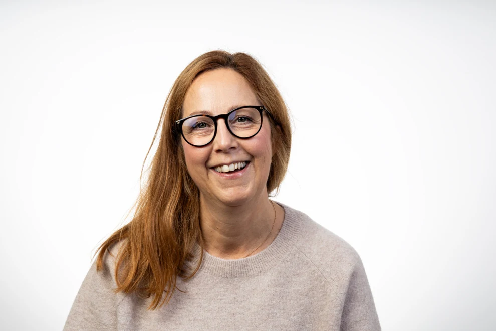 En kvinna med glasögon som ler mot kameran.