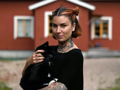 Kvinna står framför rött hus med en svart katt i famnen.