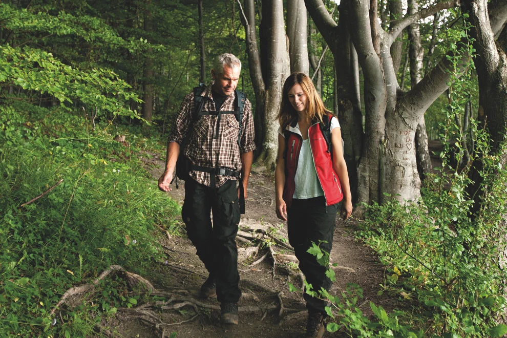 A man and a woman walking down a trail in the woods.