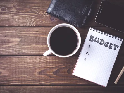 En kopp kaffe bredvid en anteckningsbok med ordet ”budget” skrivet på den.